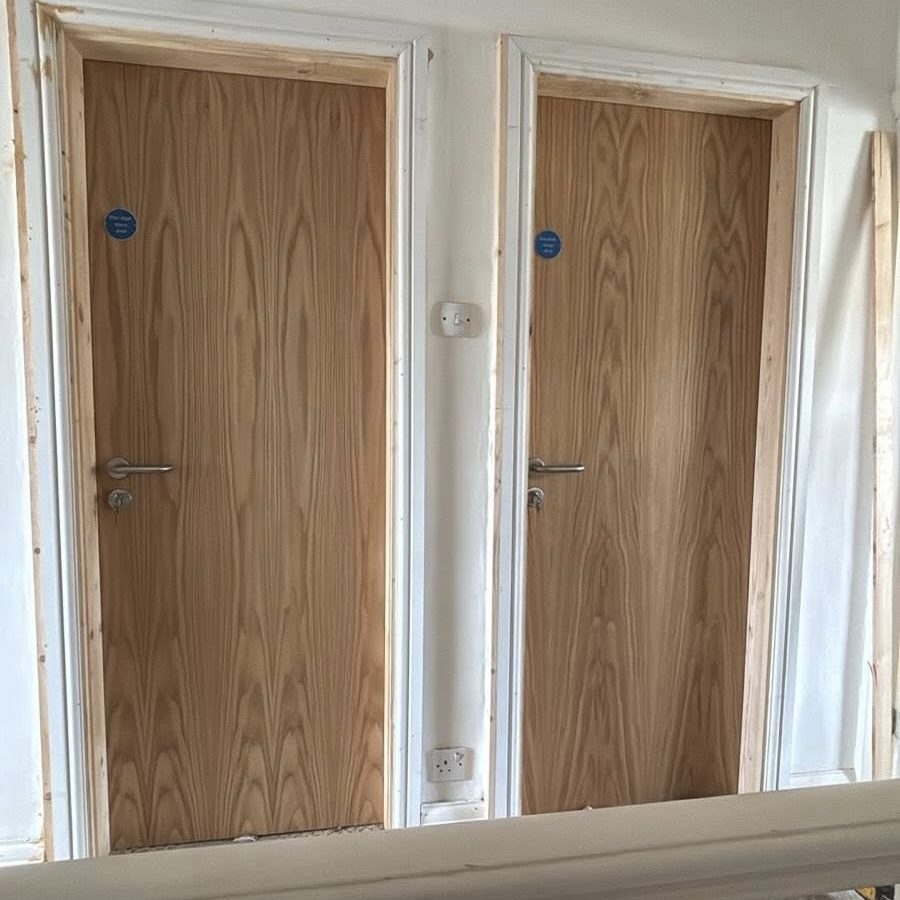 Timber Fire Door Installation Service Pair of newly installed timber fire doors in frames with statutory safety signage, showcasing our complete supply and fit service across the